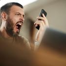 Man with beard seeming shocked by what he sees on cell phone