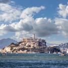 Aerial photo of Alcatraz Island prison in San Francisco Bay, boats and cloudy sky