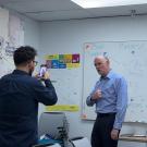 A person films UC Davis Undergraduate Admissions Executive Director Robert Penman with a smartphone as he poses in front of a whiteboard labeled “The Mythical Gen Z Slang” inside a conference room.
