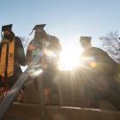 Students in caps and gowns, entering commencement, with sun behind them