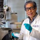 Smiling scientist in a lab coat and teal gloves holding a vial in a laboratory photo