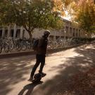 Person rides one-wheeled scooter near fall leaves.