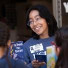 A smiling woman holding a book engages with two children outside a classroom.