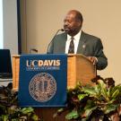 Rahim Reed speaks at podium with UC Davis banners on podium and behind him.