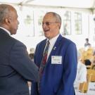 Two men in suits smiling and shaking hands at an indoor event; candid photograph.