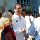 A smiling man in a white shirt converses with two people outdoors at a gathering.