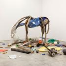Sculpture of hollow horse in beige and blue with objects scattered below