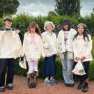 Five people wearing light-colored jackets stand in a garden with colorful flowers.