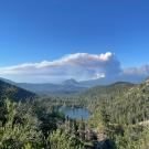 dramatic smoke plume billows over forested Castle Lake and Sierra Nevada mountains against blue sky