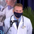 Medical student wearing face covering speaks at microphone.