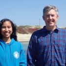 Jacquie Rajerison (left) and Professor Eric Sanford (right) at the Bodega Marine Reserve standing in front of the water and sandy coast. 