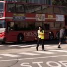 Crossing guard directing traffic, with red Unitrans bus in background.