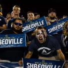 Energetic fans in blue shirts holding SHREDVILLE signs, man shouting in stadium photo