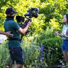 A female student talks to a camera operator and another crew member filming her in the UC Davis Arboretumcamerman and other crew member film a female student in the arboretum