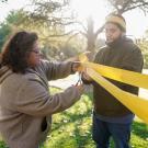Woman and Man wrap yellow ribbon around tree on the Quad