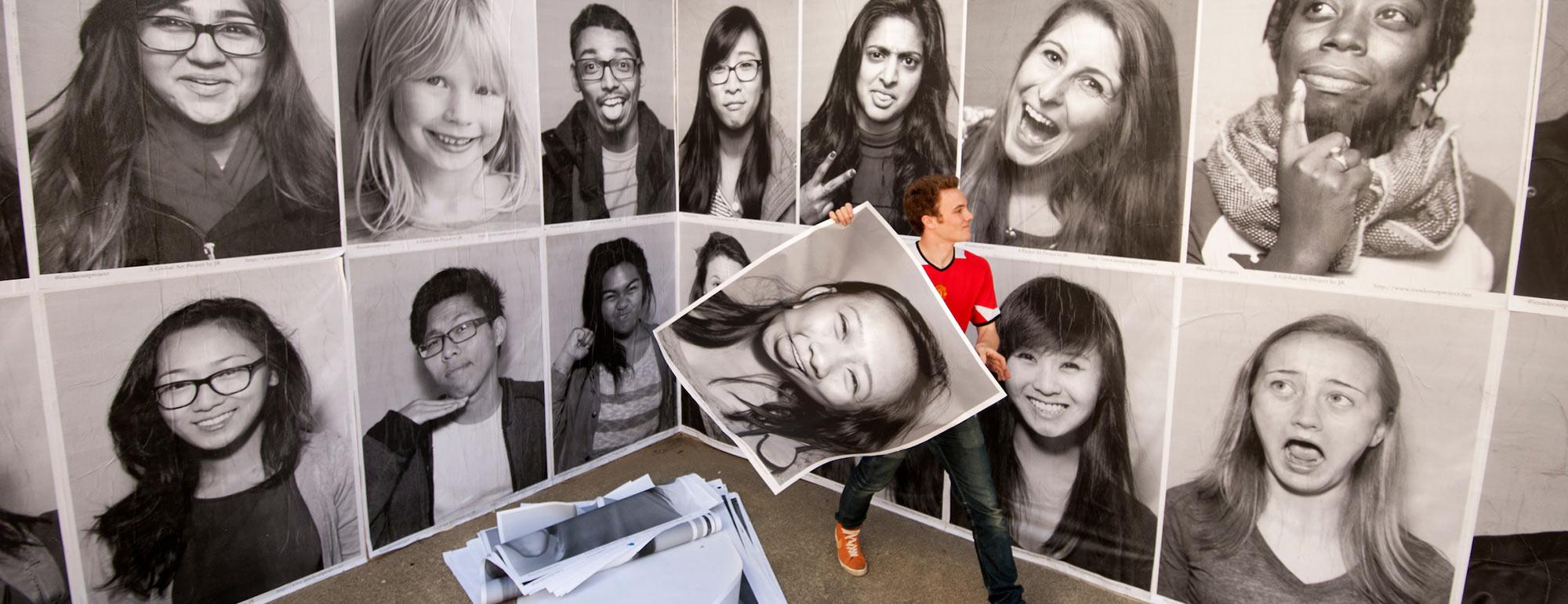 A student wall papers the Social Sciences building with artful portrait photographs