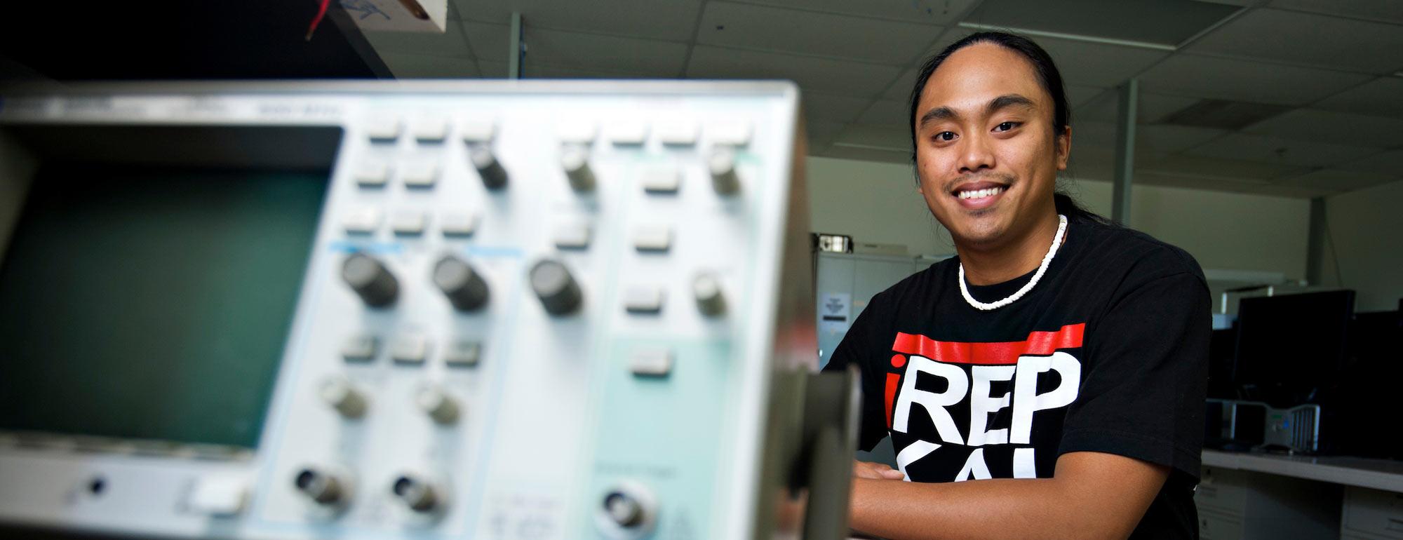 A male student poses next to some engineering lab equipment