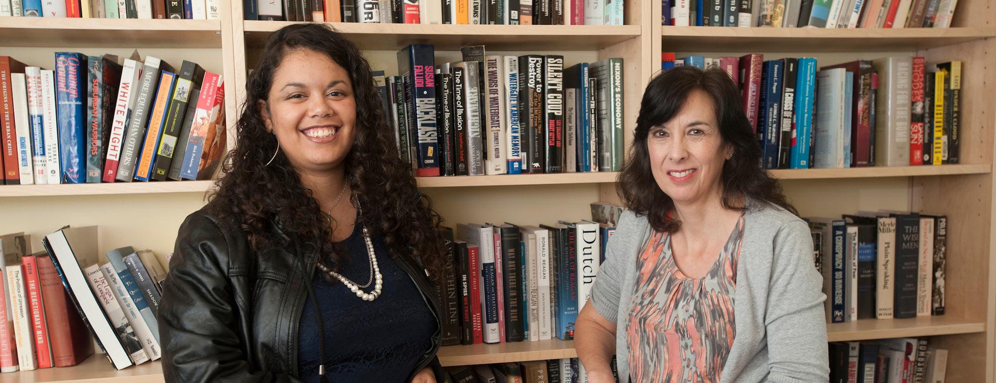 A PHD candidate and a History professor pose in front of a book shelf.
