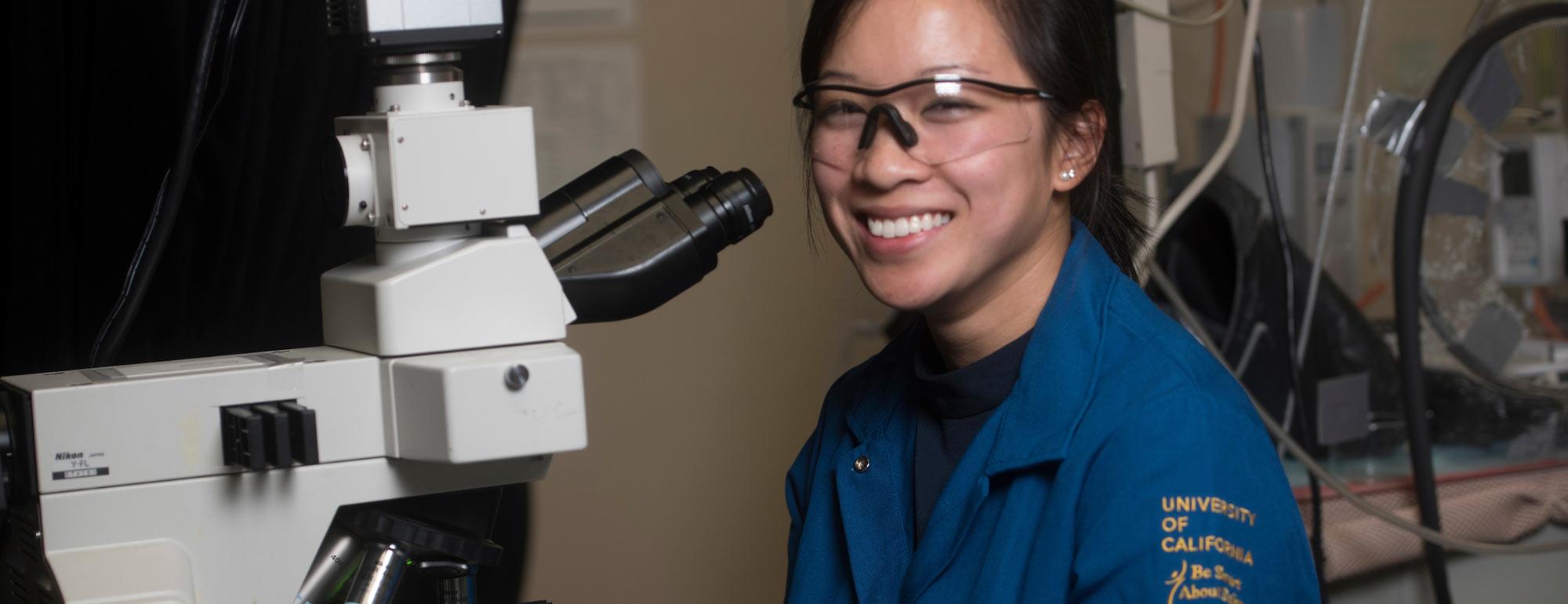 A female student smiling next to her microscope