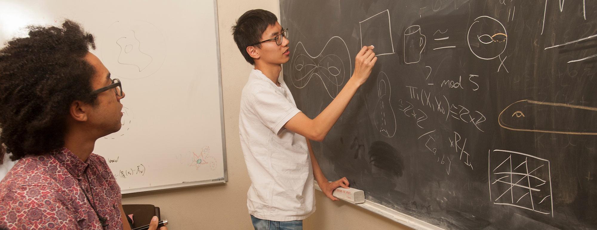 A student solves a complex equation on a blackboard