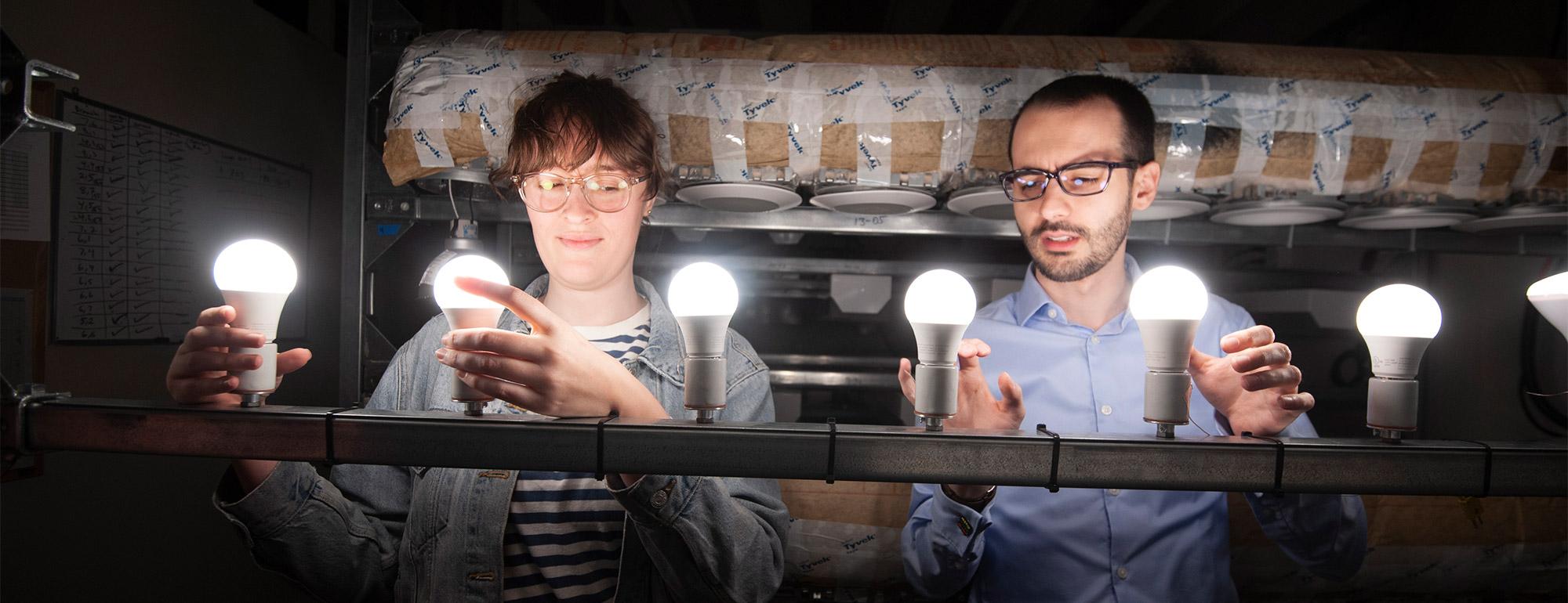 two student research partners with a row of lightbulbs collaborating on a project involving lighting