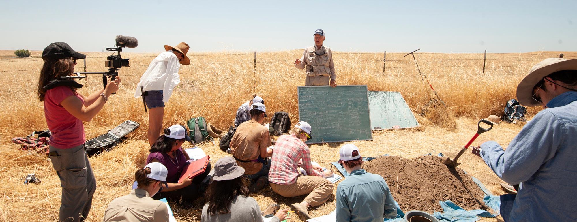 a professor conducting a soil science class with students outside
