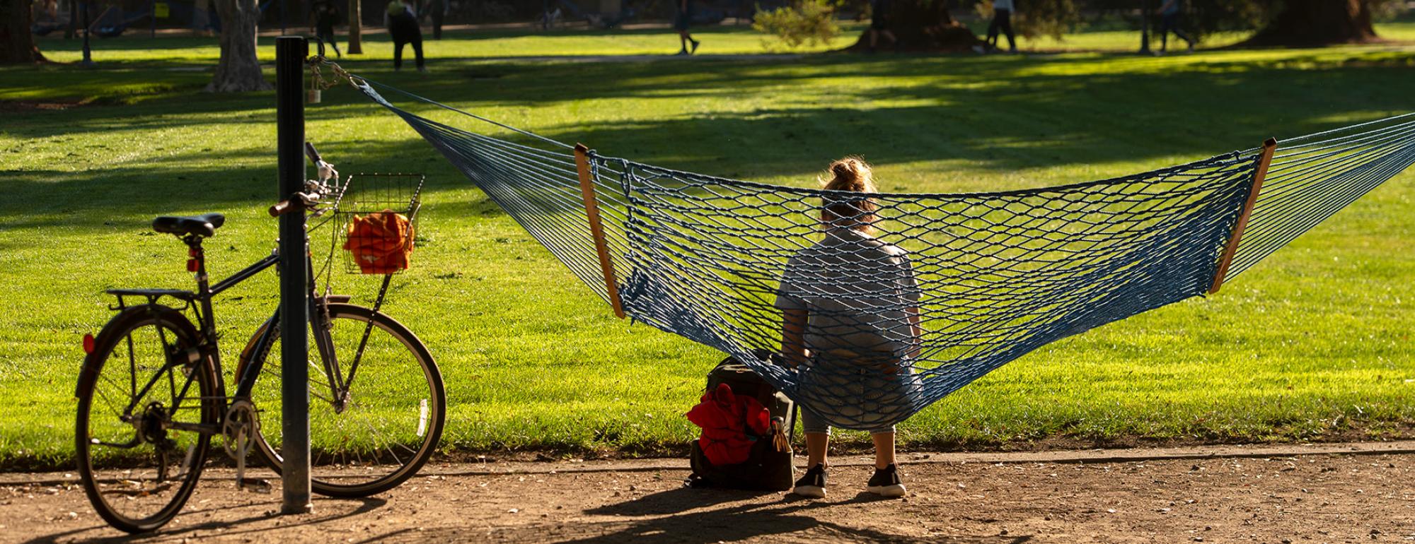 student sitting in a hammock next to a bike at the quad