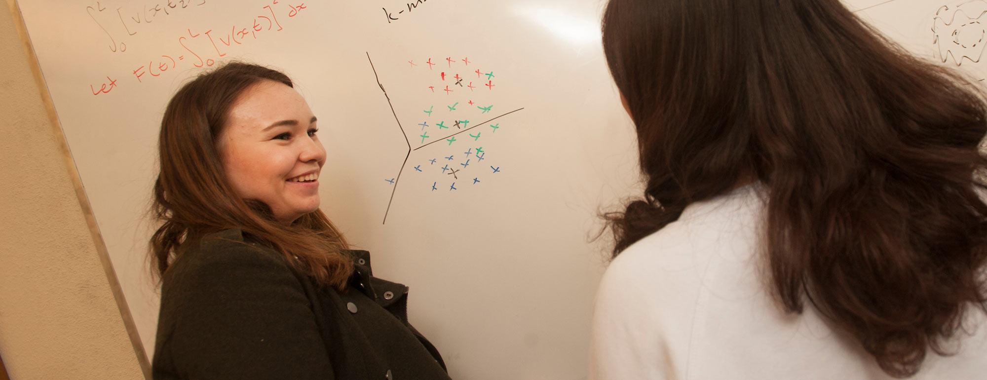 Two female students discuss a math problem at a whiteboard
