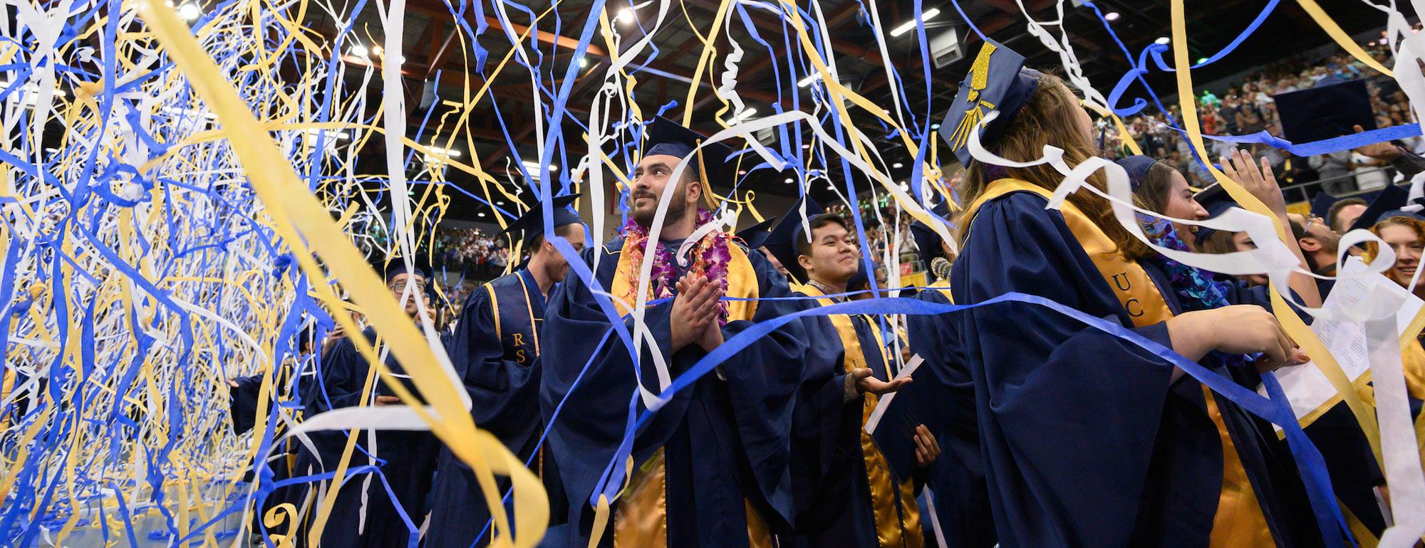 Students celebrating at commencement while streamers fall from the ceiling