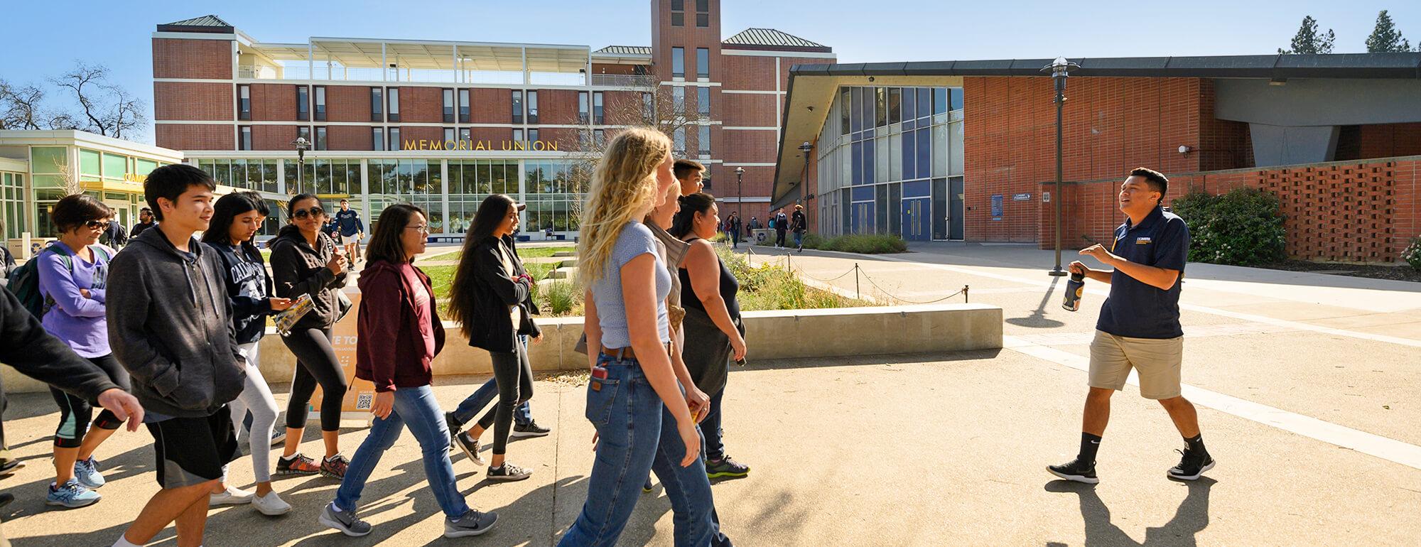 A UC Davis tour guide walks backward through campus highliting campus sights to his audience