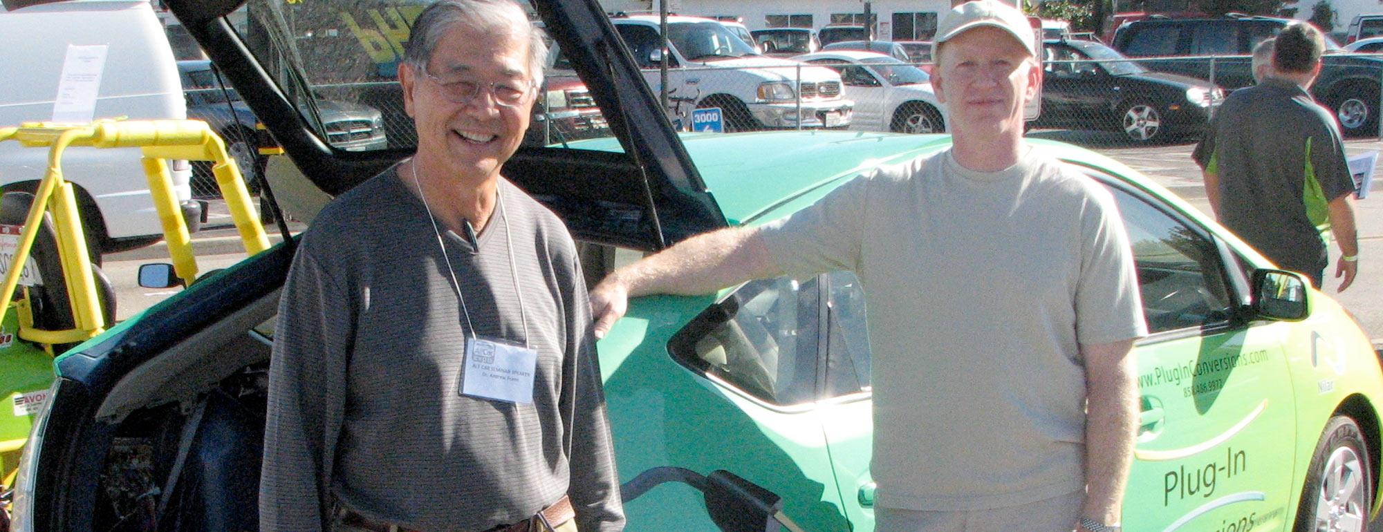 Two men pose next an electric car