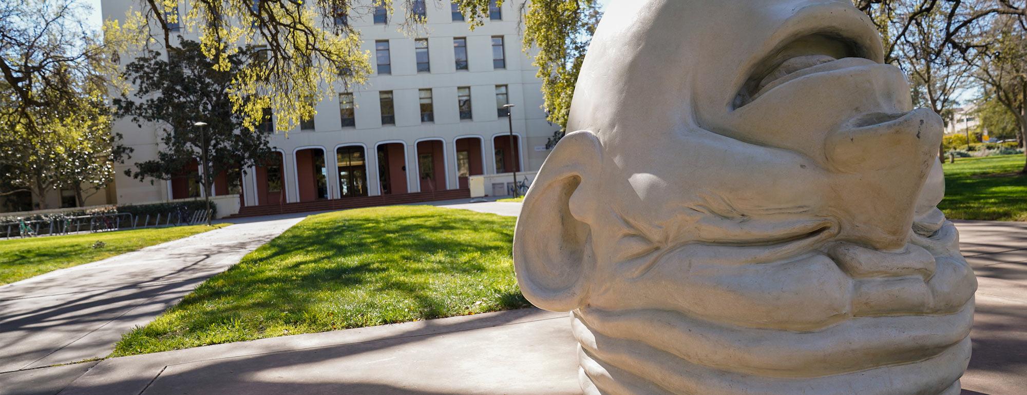 An egghead sculpture on its top maniancally laughs outside of Mrak Hall