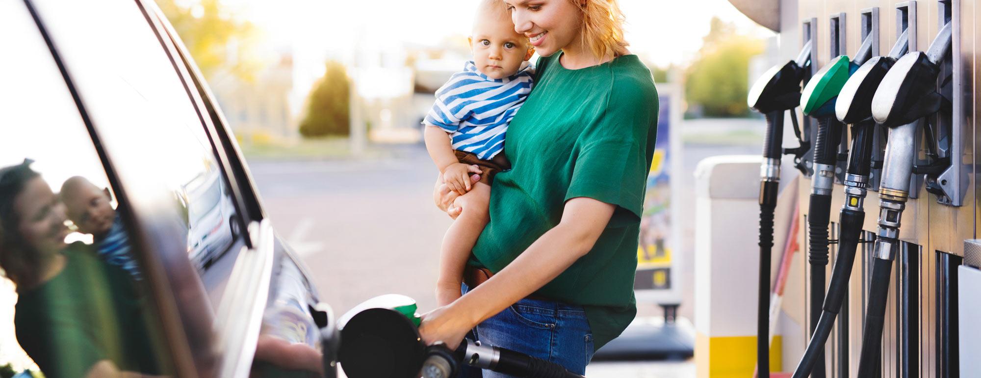 A mother holding a baby gasses up her car at the gas station