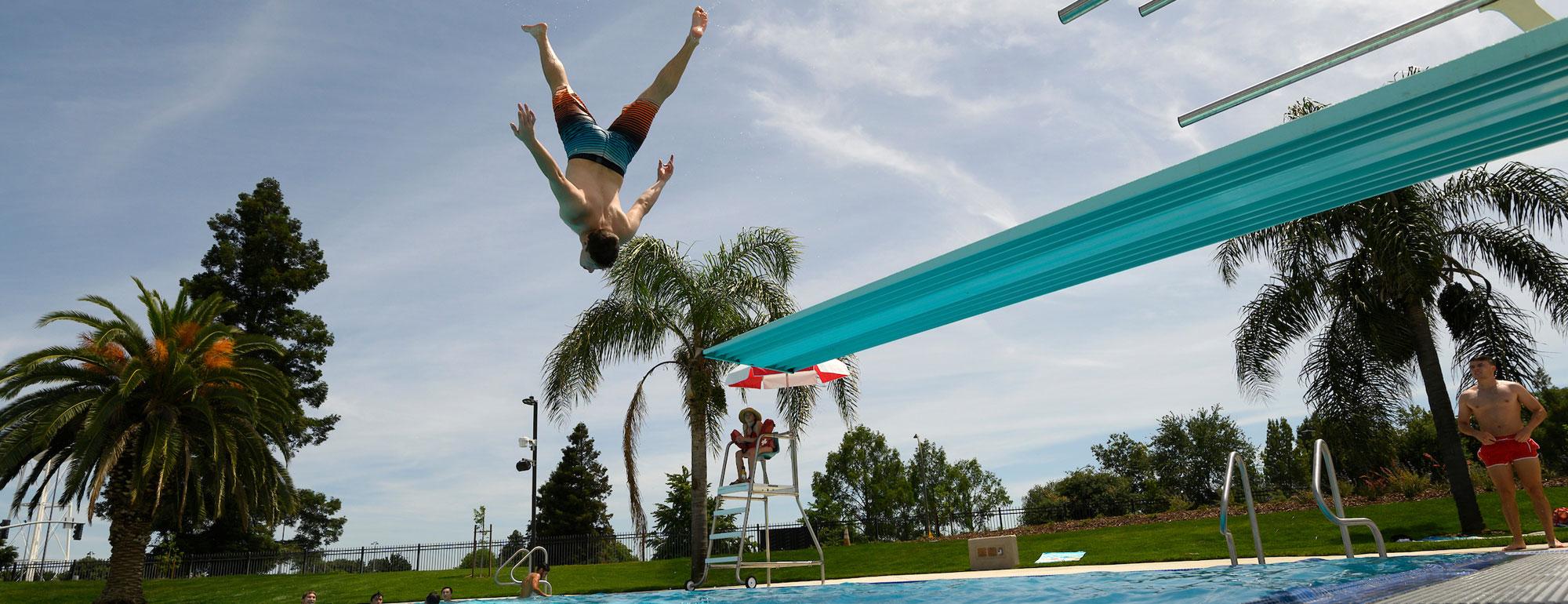 A student doing an acrobatic jump of of the diving board at the UC Davis Recreation Pool