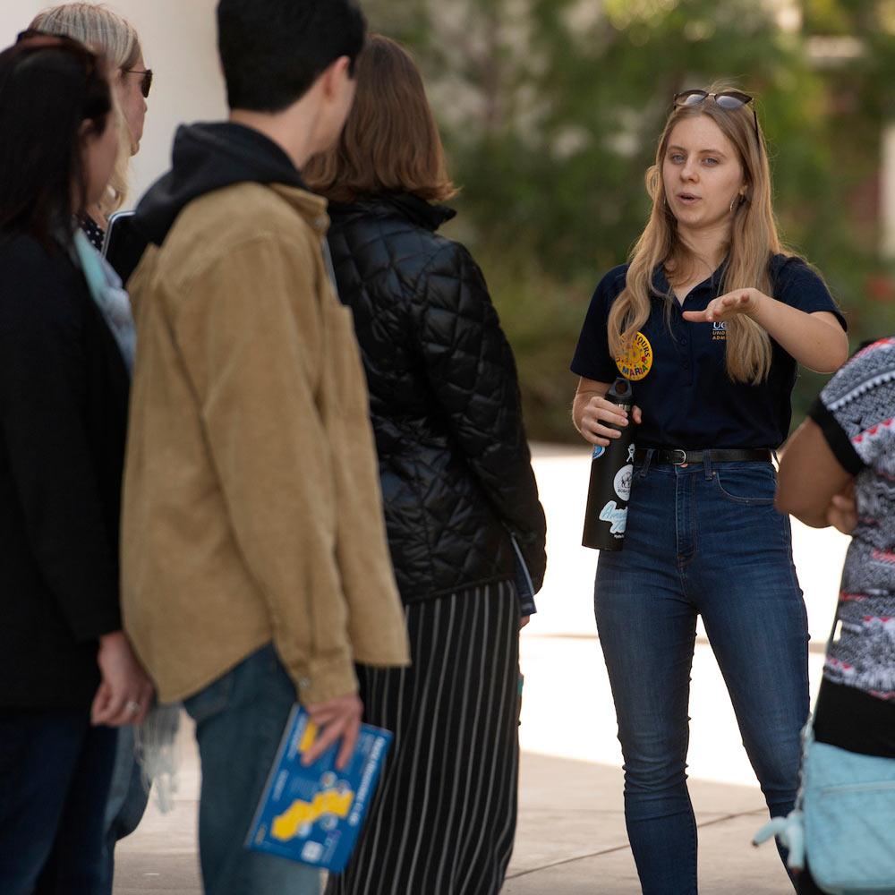 A female student tour guide leads a group of prospective students and parents through the UC Davis campus