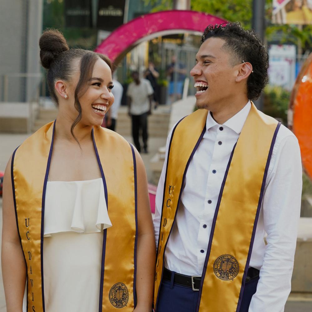 Two graduates laugh while sharing a moment outside of the Golden 1 center