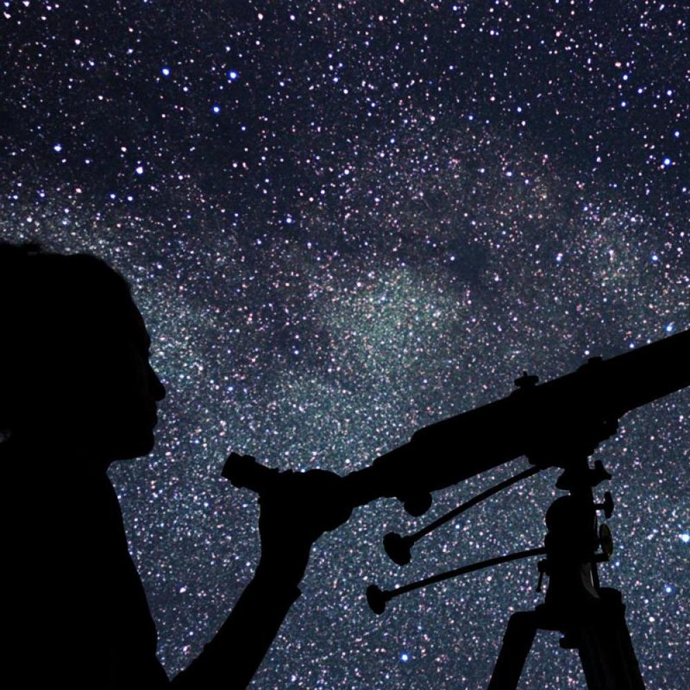 A person pearing through a telescope at a star-filled sky