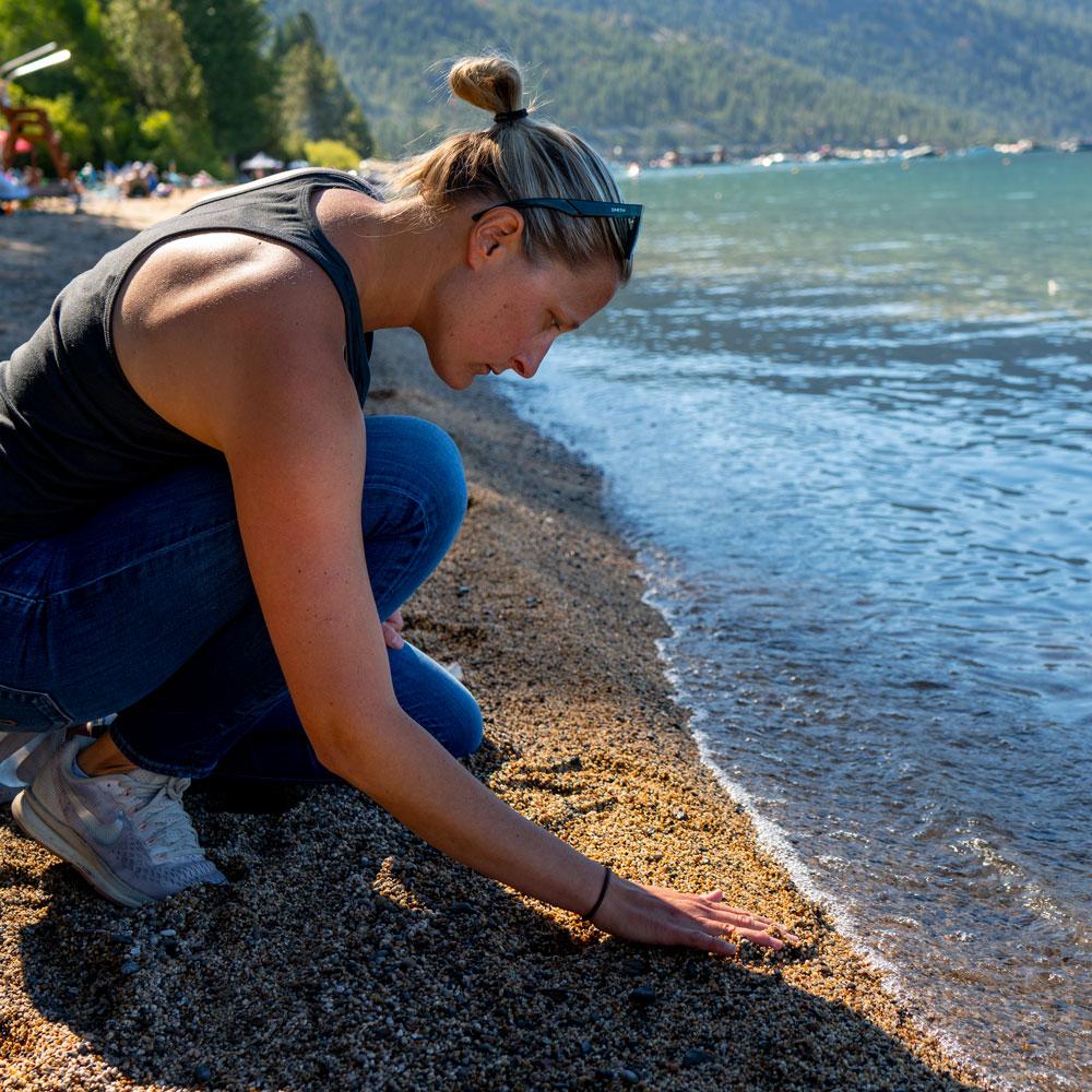 Student crouching at the shore of a beach in Lake Tahoe doing research for the Tahoe Environmental Research Center