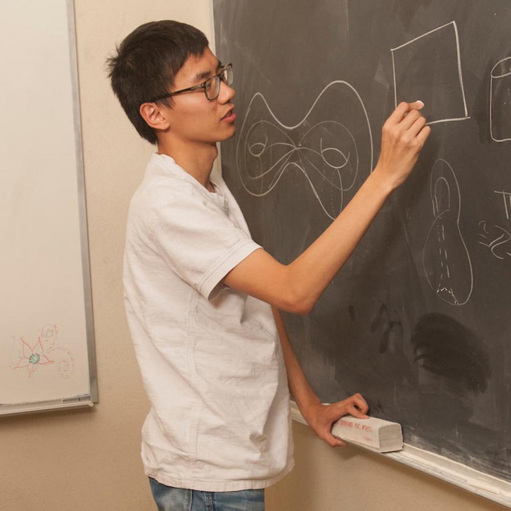 A student solves a complex equation on a blackboard