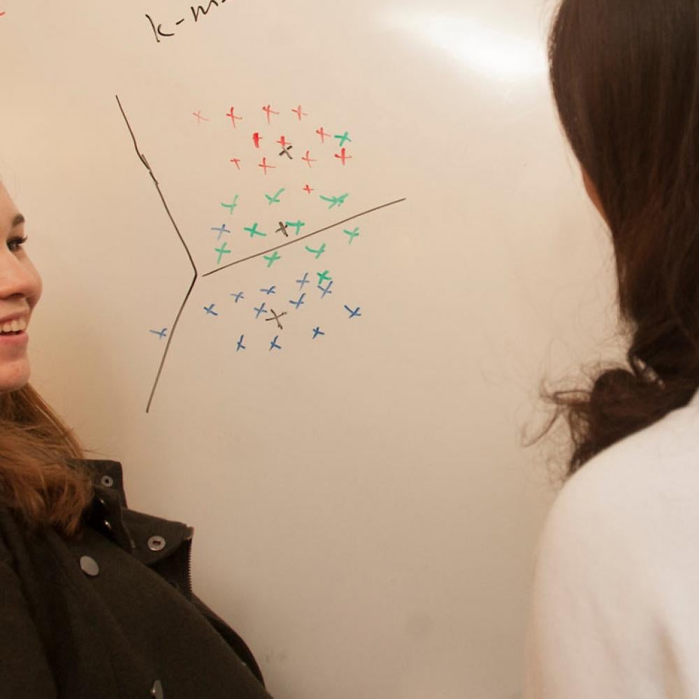 Two female students discuss a math problem at a whiteboard