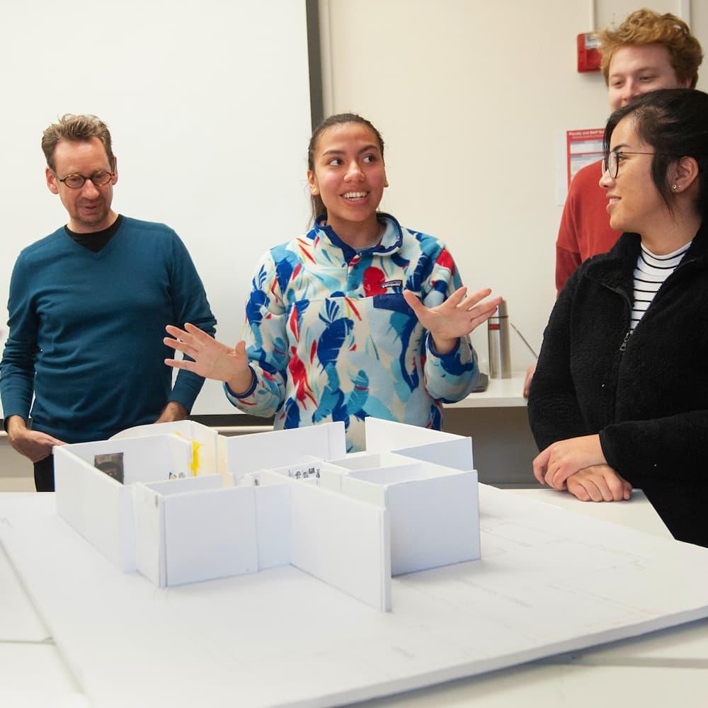 three students and a professor looking at a model of a building in a design class.