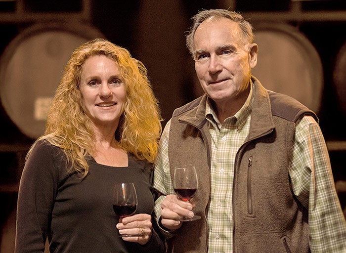 Carol and John Franzia standing in a winery with barrels behind them