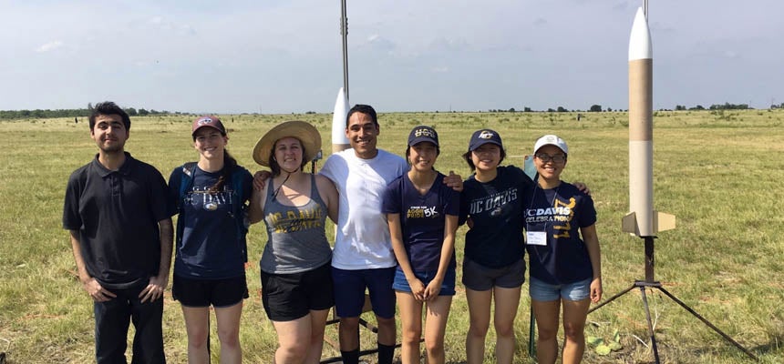 Students stand in a field next to their space rocket