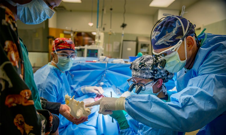 A number of doctors and nurses in gowns and masks in an operating room