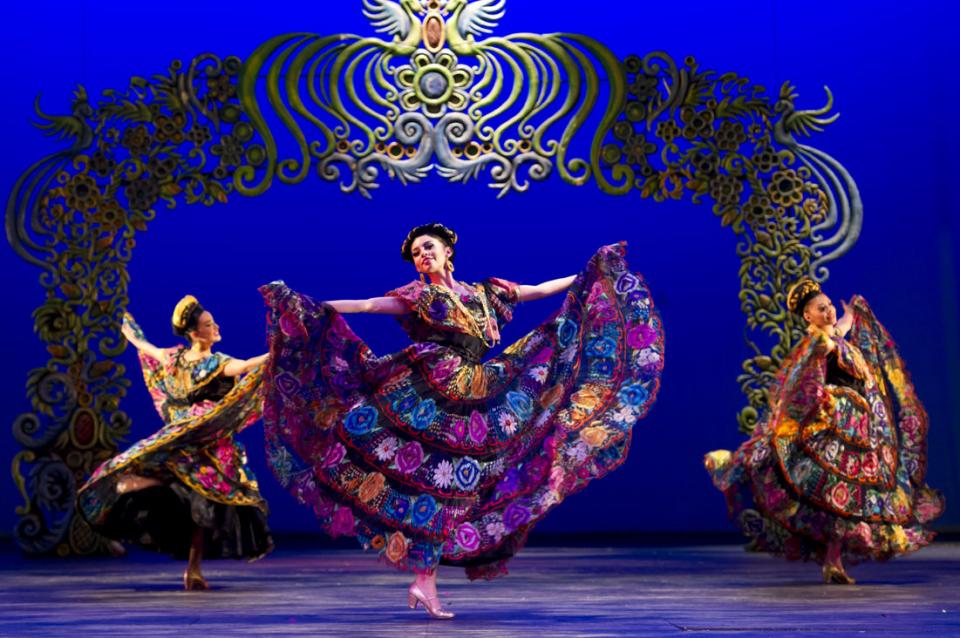 Three female dancers weraing colorful traditional Mexican dresses.