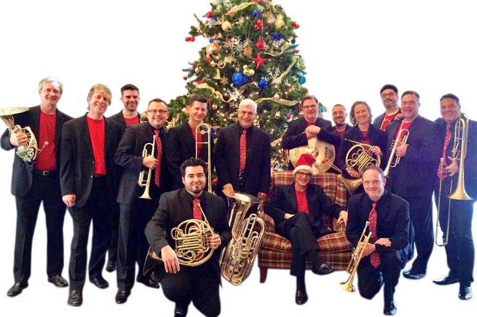 Members of Boston Brass posing with their musical instruments in front of a Christmas tree.