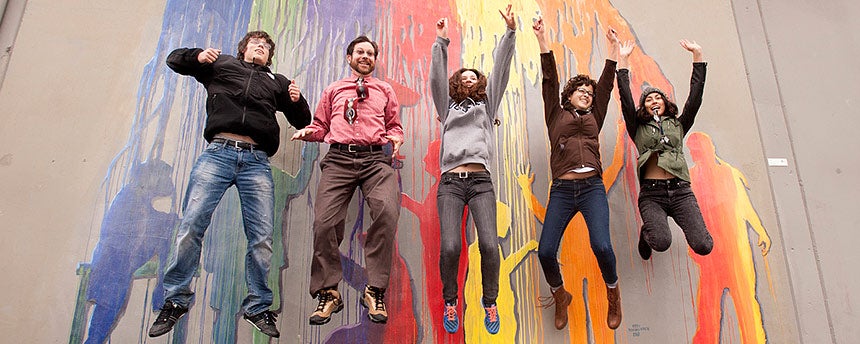 Five people jumping in the air in front of a mural of paint splashes