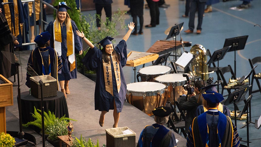A graduate raises her arms as she crosses a graduation stage