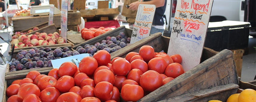 Wooden boxes of tomatoes, plums and apples displayed at a farmers market.