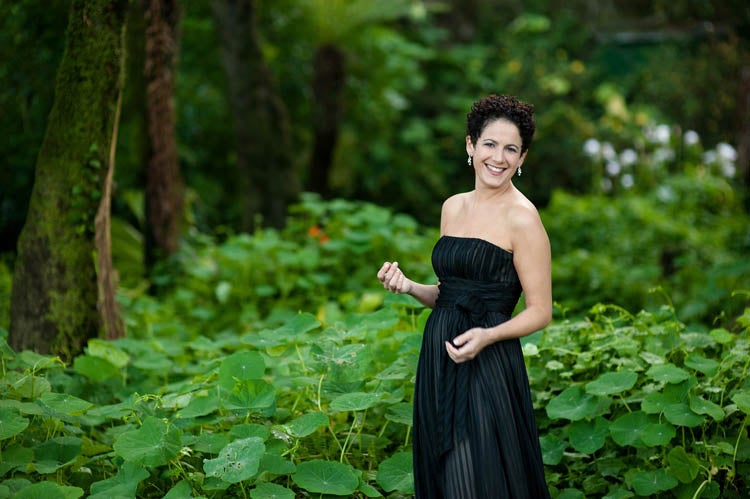 Ane Moss in a black dress standing in a lush green forest.
